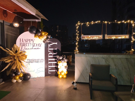 Black and gold birthday decoration at home with balloon backdrop, elegant signage and fairy lights