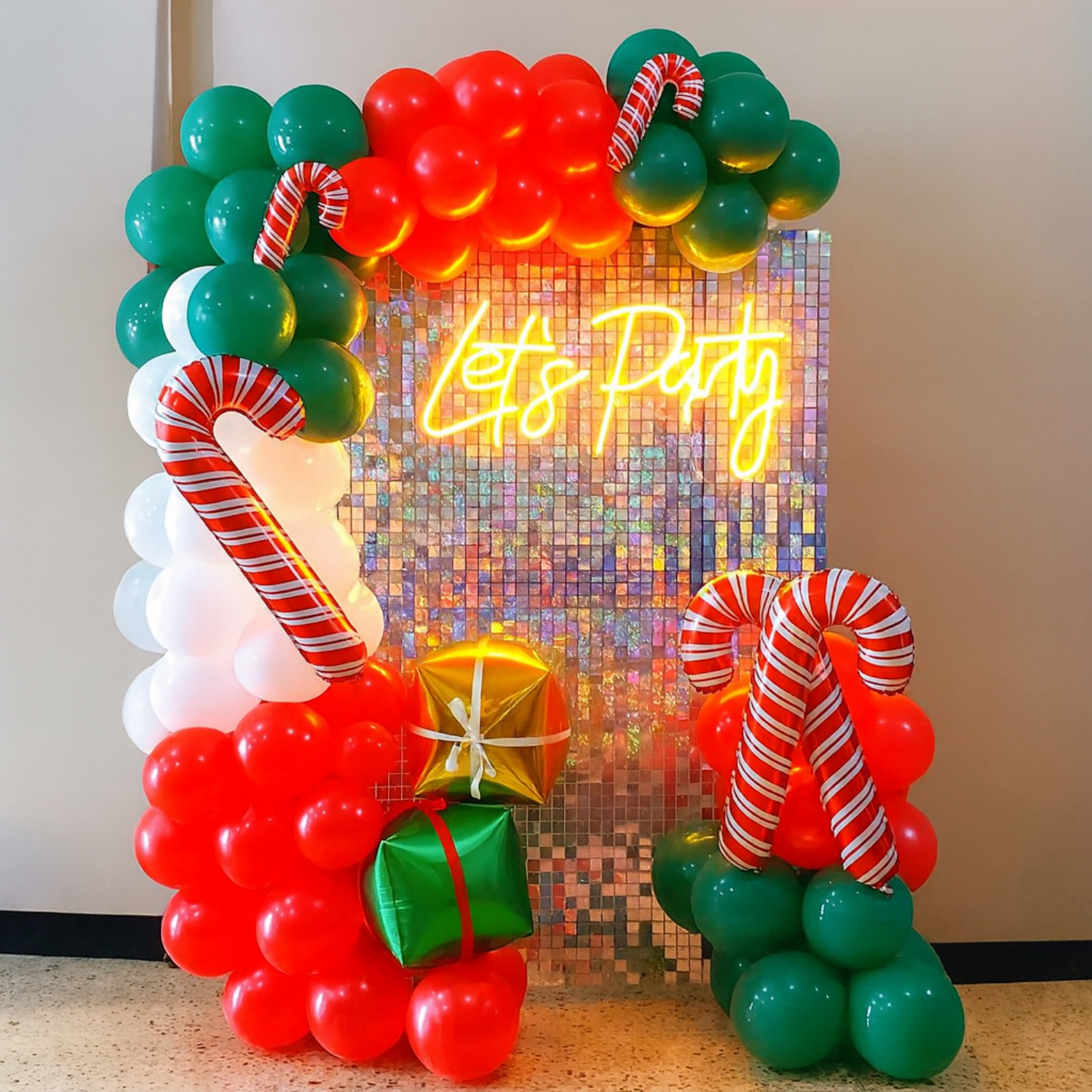 Christmas balloon decoration with red, green, and white balloons, candy canes, gift boxes, and a “Let’s Party” neon sign backdrop.