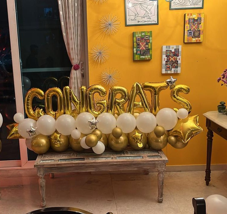 Congrats balloon setup featuring gold letters and white balloon flowers with golden accents.