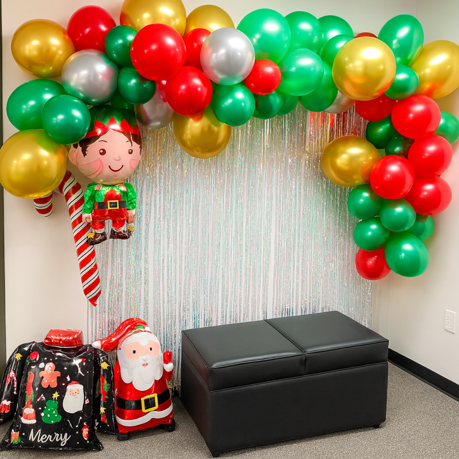 Christmas balloon decoration with red, green, and gold balloon arch, Santa and elf balloons, and tinsel backdrop.