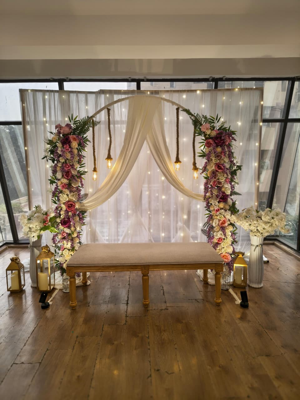 Floral Roka backdrop decor with pastel flowers, draped fabric, warm lights, lanterns and seating bench