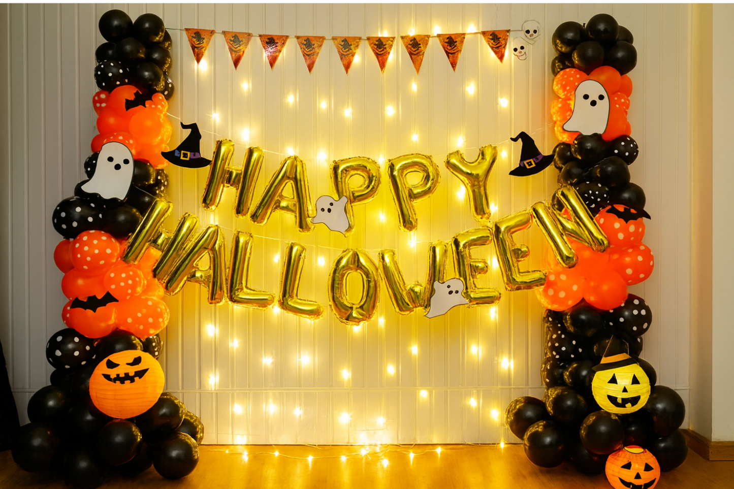 Happy Halloween balloon decoration with black and orange balloons, fairy lights, and ghost cutouts.
