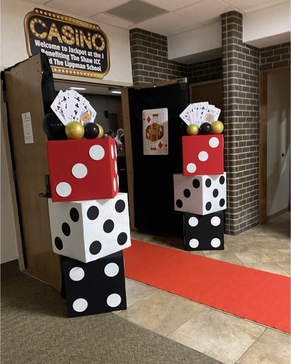 casino night entrance decoration with giant dice, playing cards, gold balloons, and red carpet setup for party event