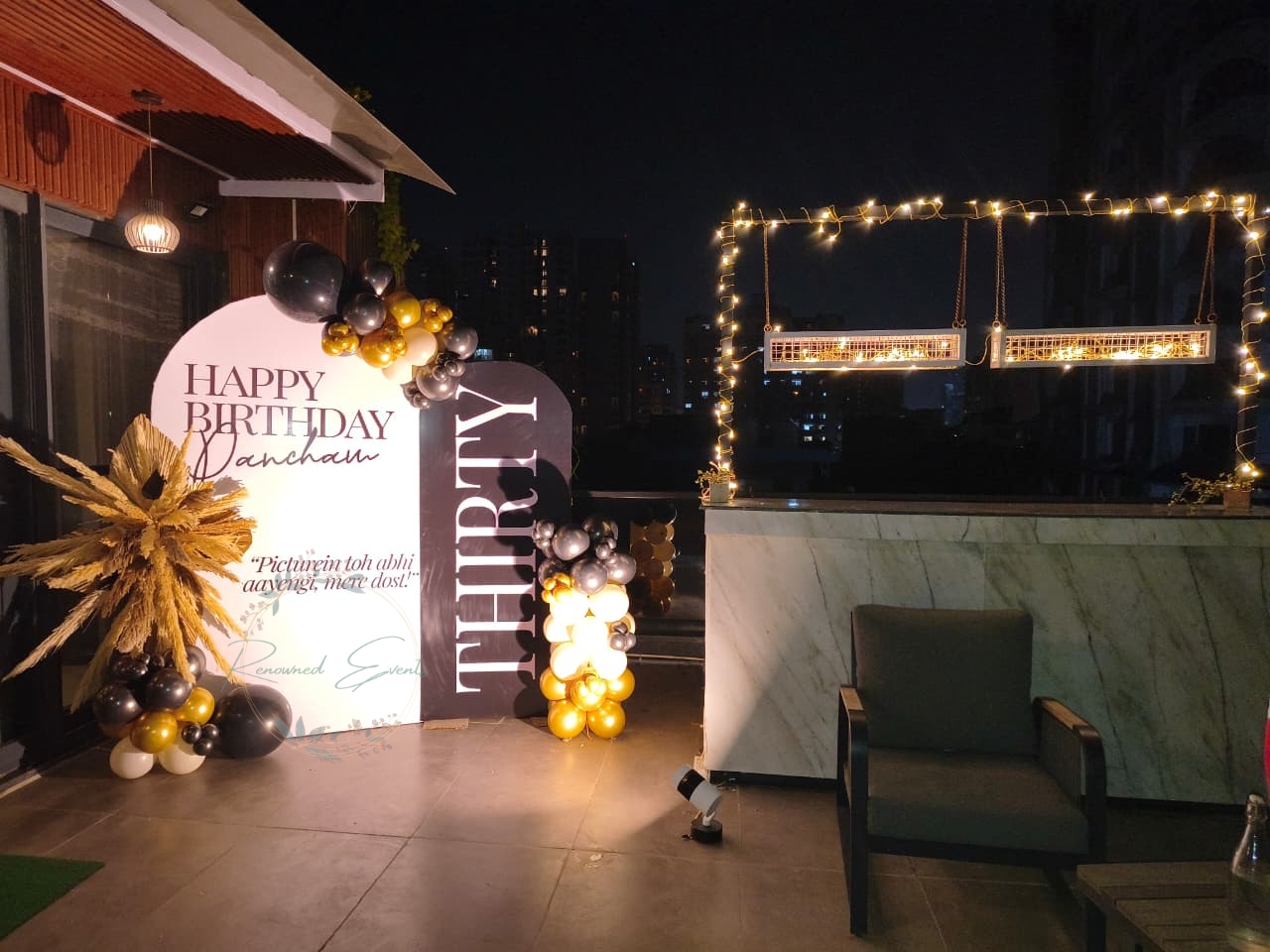 Black and gold birthday decoration at home with balloon backdrop, elegant signage and fairy lights