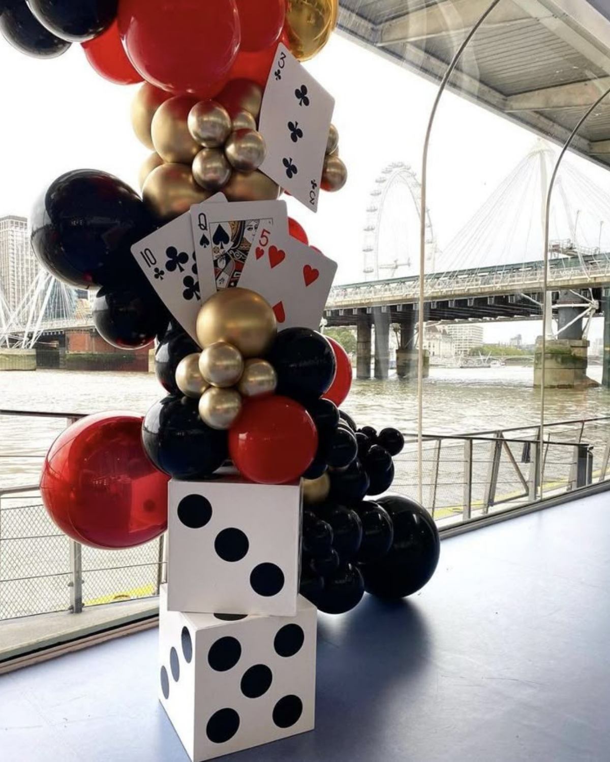 Elegant casino theme balloon decoration featuring red, black, and gold balloons with playing cards and dice props, perfect for a Vegas or casino night party backdrop.