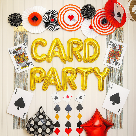 Card party wall decoration with gold balloons, playing cards, and paper fans in red, black, and white.