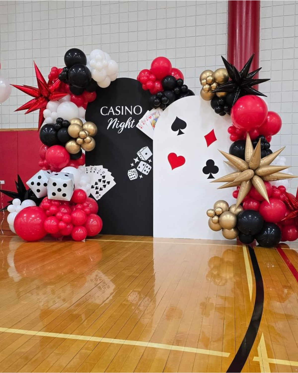 Casino night balloon decoration with red, black, gold, and white balloons, dice props, playing cards, and themed backdrop.