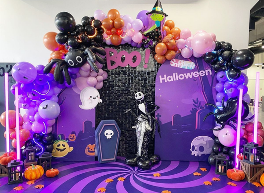 Halloween 2024 balloon backdrop with skeleton prop, giant spider balloons, ghosts, pumpkins and purple balloon arch decoration.