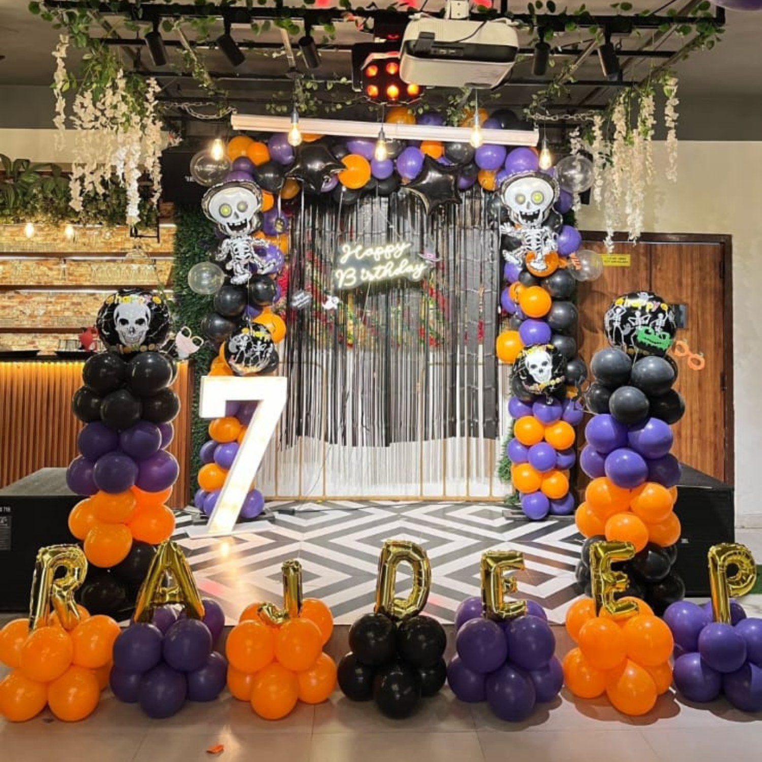 Halloween birthday stage decoration with balloon arch, skeleton props, happy birthday backdrop and customized balloon letters for kids’ party.