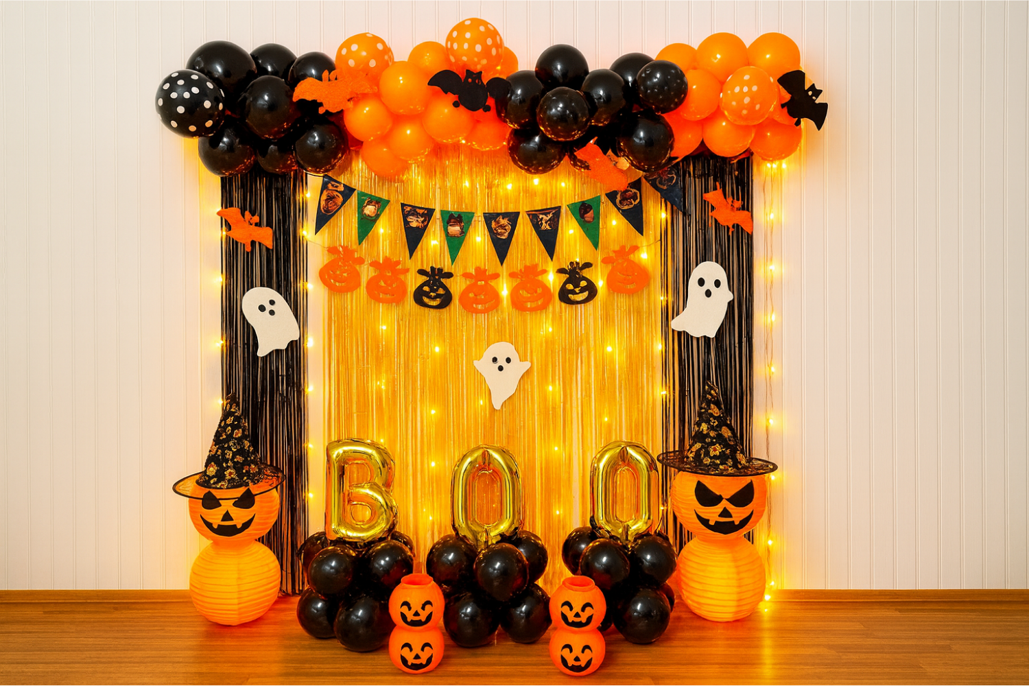Halloween “BOO” balloon backdrop with black and orange balloons, fairy lights, ghosts, and pumpkin lanterns.