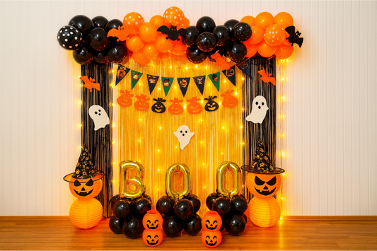 Halloween “BOO” balloon backdrop with black and orange balloons, fairy lights, ghosts, and pumpkin lanterns.
