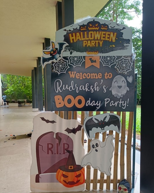 Halloween party welcome board decorated with ghost, bat, pumpkin cutouts and spooky tombstone design.