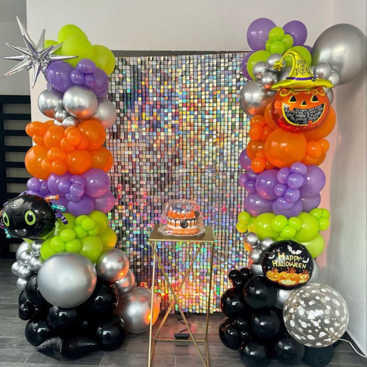 Halloween balloon backdrop with silver sequin wall, pumpkin balloons, colorful balloon pillars and cake table for party decoration.