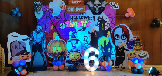 Halloween birthday backdrop with zombie cutouts, ghost props, pumpkins, cartoon characters and balloon clusters for party decoration.