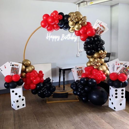 Casino theme birthday balloon arch in red, black, and gold with dice props and playing card decorations.