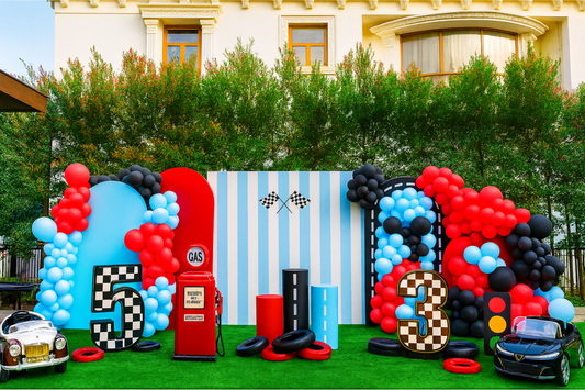 Race car-themed birthday decoration with red, blue, and black balloons, checkered numbers, gas station prop, and toy cars.