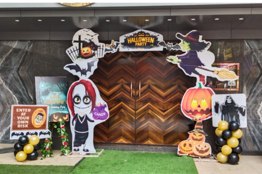 Spooky Halloween party entrance decoration with witch cutout, pumpkins, cartoon props and balloon décor—perfect for parties and themed events.