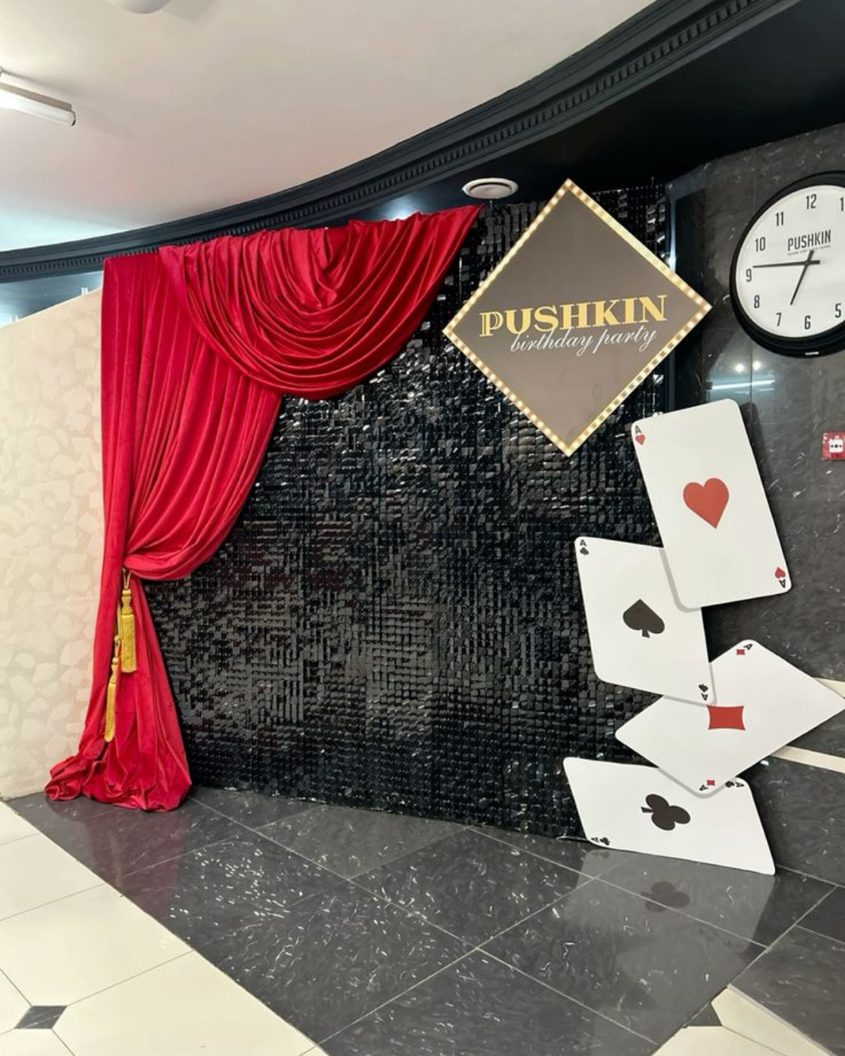Casino-themed birthday party backdrop with black sequin wall, red velvet curtain, and large playing card props — perfect for luxury Vegas-style celebrations.